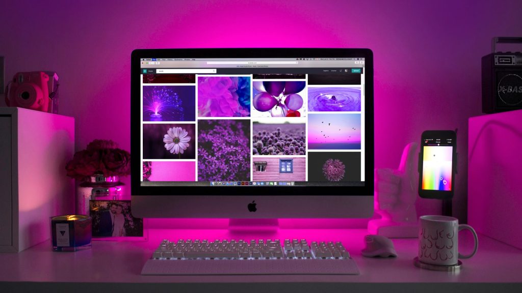 dark purple and pink light coming from a computer on a desk with photos on the screen
